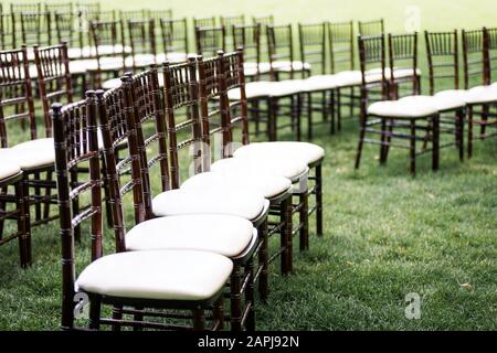 Rows of padded wooden chairs setup for outdoor wedding ceremony Stock Photo