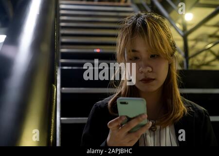 Blond hair woman with fringe in black and white clothes sitting on the stair looking at her smartphone to read the massage from her couple. Stock Photo