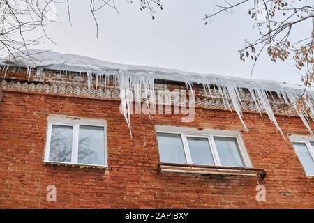 many large icicles hanging from the roof of a brick house Stock Photo