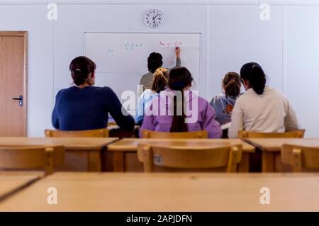 Pupils in classroom from behind with teacher writing on whiteboard Stock Photo