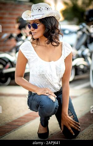 African American Woman with sunglasses and white straw cowboy hat with street motorcycle and red brick wall diffused in background Stock Photo