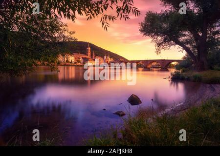 Heidelberg, Germany, dreamy sunset colors over the Neckar river with the Old Town and Bridge, framed by silhouettes of trees Stock Photo