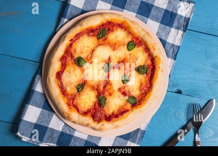 Whole pizza Margherita on oven plate on a bavarian napkin and blue table. Mozzarella pizza freshly baked. Oktoberfest food. Melted cheese pizza. Stock Photo