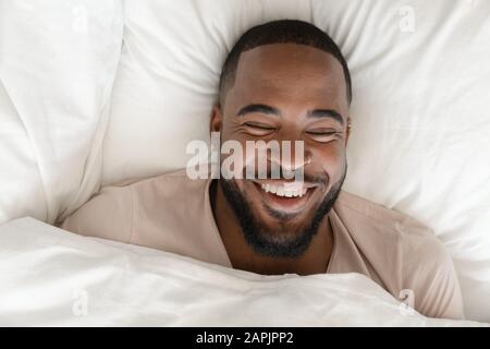 View from above laughs handsome african guy lying in bed Stock Photo