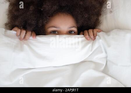 Cute little african girl hides behind blanket looking at camera Stock Photo