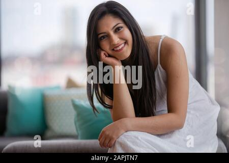 Cute adorable beautiful young Indian american woman at home sitting on sofa, smiling, cheerful, femininity, pretty face, portrait Stock Photo