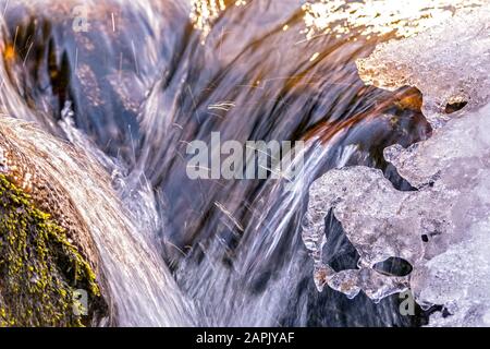 Ice on fast flowing mountain river and sparkling drops of water Stock Photo