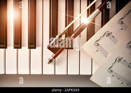 Bow with sheet music on piano keys top. Concept of interpretation of piano music and string instruments. Top view. Horizontal composition. Stock Photo