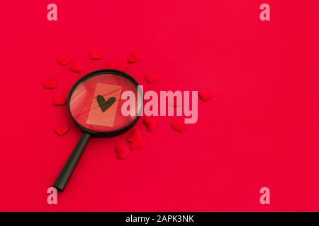 Black heart through a magnifying glass among red hearts on red background. Valentine day concept, searching for special love concept. Stock Photo