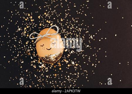 Creative easter egg with cute face and sleepy eyes on black background with golden glitter confetti. Stock Photo