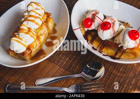 Banana split topped with cherries and bread pudding desserts sitting on a wooden table. Stock Photo