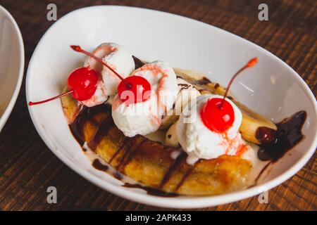 Banana split topped with cherries and bread pudding desserts sitting on a wooden table. Stock Photo