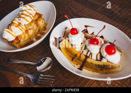 Banana split topped with cherries and bread pudding desserts sitting on a wooden table. Stock Photo