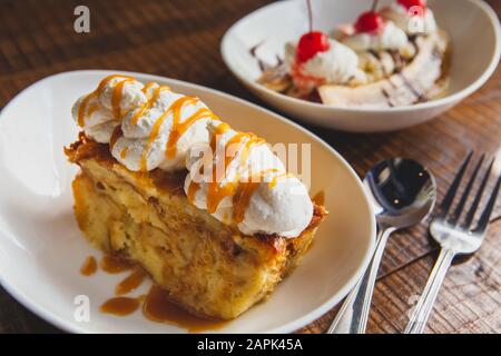 Banana split topped with cherries and bread pudding desserts sitting on a wooden table. Stock Photo