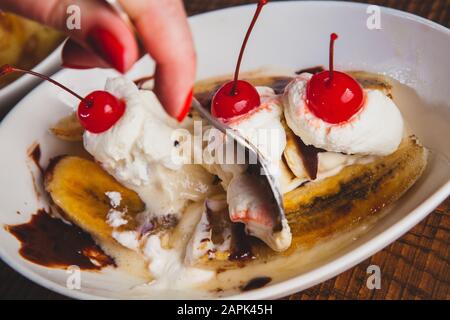 Banana split topped with cherries and bread pudding desserts sitting on a wooden table. Stock Photo