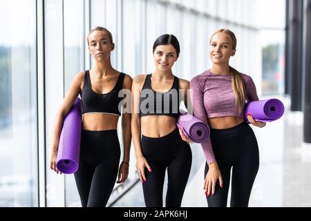 Three women talking with yoga mats standing in gym Stock Photo
