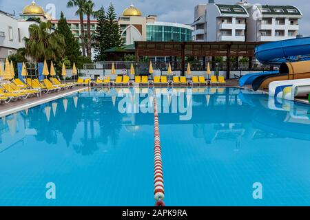 Turkey Alanya May 05, 2019: A big outdoor pool with a lot of yellow lounges and umbrellas on both sides in the water park on a sunny day. Stock Photo