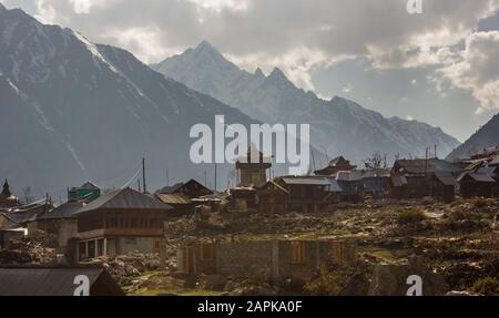 The ancient wooden temple and the houses of the Chitkul village set against the backdrop of the high snow covered Himalayan mountains surrounding them Stock Photo