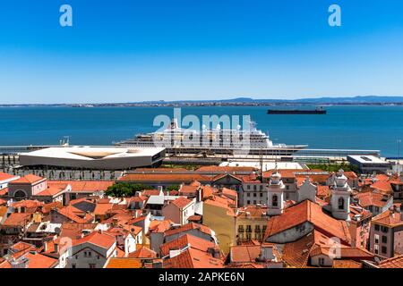 Cruise ship docked at the coast of Lisbon with rooftops of Alfama in the foreground and tanker in the background. Stock Photo