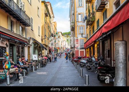 Tourists and local French enjoy an afternoon at shops and sidewalk cafes on a narrow street in Old Town Vieux Nice, France. Stock Photo