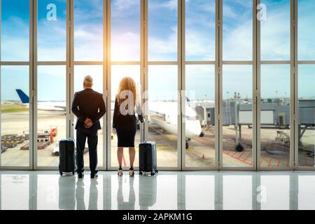 Couple of Businessman and businesswoman standing together with baggage near the window at the departure area at the terminal in international airport. Stock Photo
