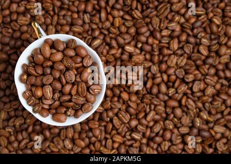 A white cup is peppered with beans against the background of coffee beans. Copy space. Stock Photo
