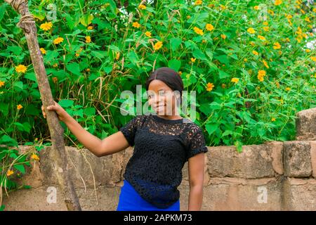 beautiful african girl standing near a fence with tree marigold sunflowers growing over Stock Photo