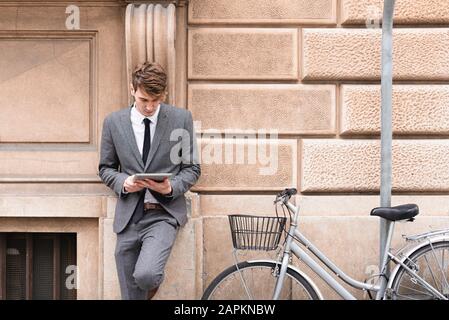 Young businessman leaning at facade looking at digital tablet Stock Photo