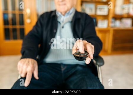 Hand of senior man sitting in wheelchair using remote control, close-up Stock Photo