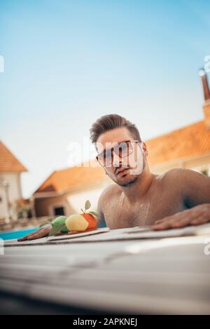 Young man in sunglasses resting on edge of swimming pool