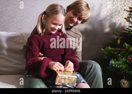 Blonde girl and opening Christmas present, Father behind her Stock Photo