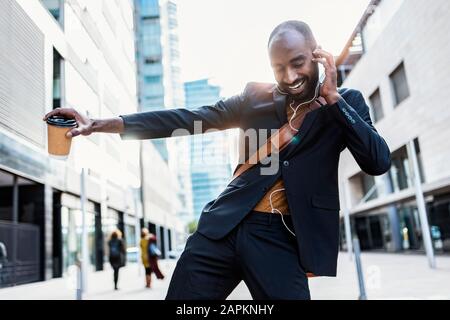 Portrait of happy young businessman dancing on the street while listening music with earphones Stock Photo