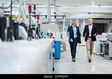 Two businessmen walking and talking in a factory Stock Photo