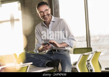 Happy mature businessman with cell phone in office Stock Photo