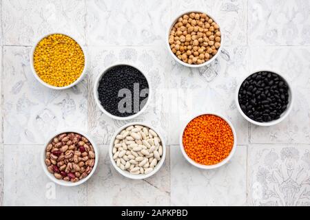 Various legumes in bowls: chickpeas, cannellini beans, quail beans, black beans, yellow lentils, red lentils, black lentils Stock Photo