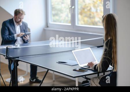 Businessman and businesswoman working at table tennis table in office Stock Photo
