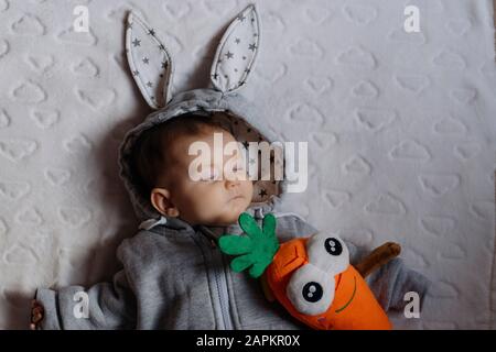 Portrait of sleeping baby girl in a rabbit hoodie lying on white blanket Stock Photo