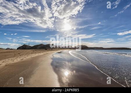New Zealand, Wellington Region, Castlepoint, Sun shining over sandy coastal beach of Pacific Ocean Stock Photo