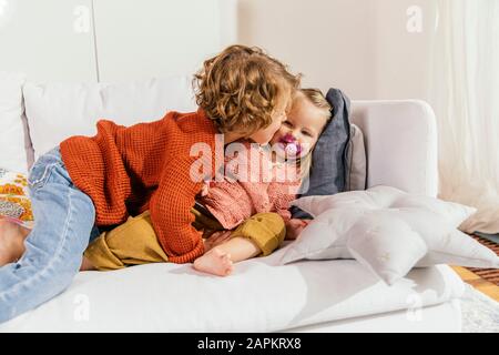 Two little sisters cuddling on couch at home Stock Photo