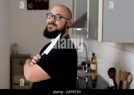 Portrait of smiling bearded man holding kitchen knife in kitchen Stock Photo