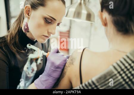 female tattooist tattooing upper arm of female customer Stock Photo