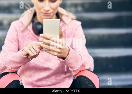 Sporty woman sitting on stairs, using smartphone Stock Photo