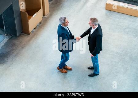 Two businessmen shaking hands in a factory Stock Photo