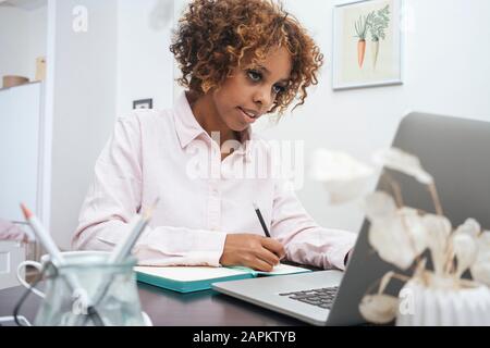 Young woman working at home taking notes and using laptop Stock Photo