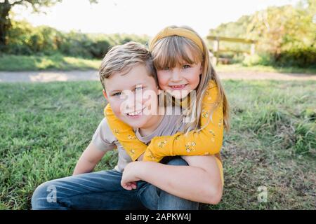 Portrait of smiling little girl head to head with her older brother on a meadow Stock Photo