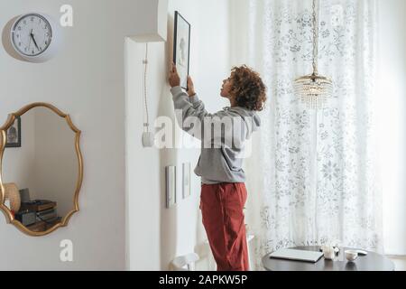 Young woman hanging up picture at home Stock Photo