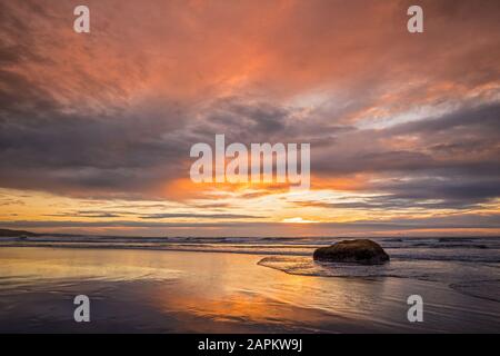 New Zealand, Tongaporutu, Cloudy sky over sandy coastal beach at orange dusk
