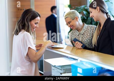 Two smiling businesswomen talking to woman at reception desk Stock Photo