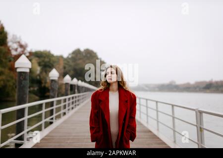 Portrait of young woman wearing red coat on a bridge during rainy day