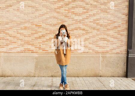 Young woman with camera taking pictures in front of a brick wall Stock Photo